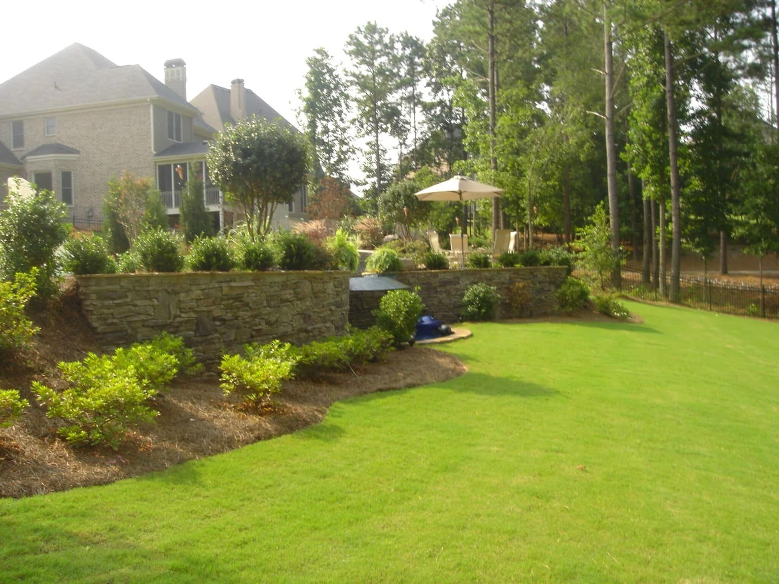 Backyard Garden With Stone Wall And Green Lawn